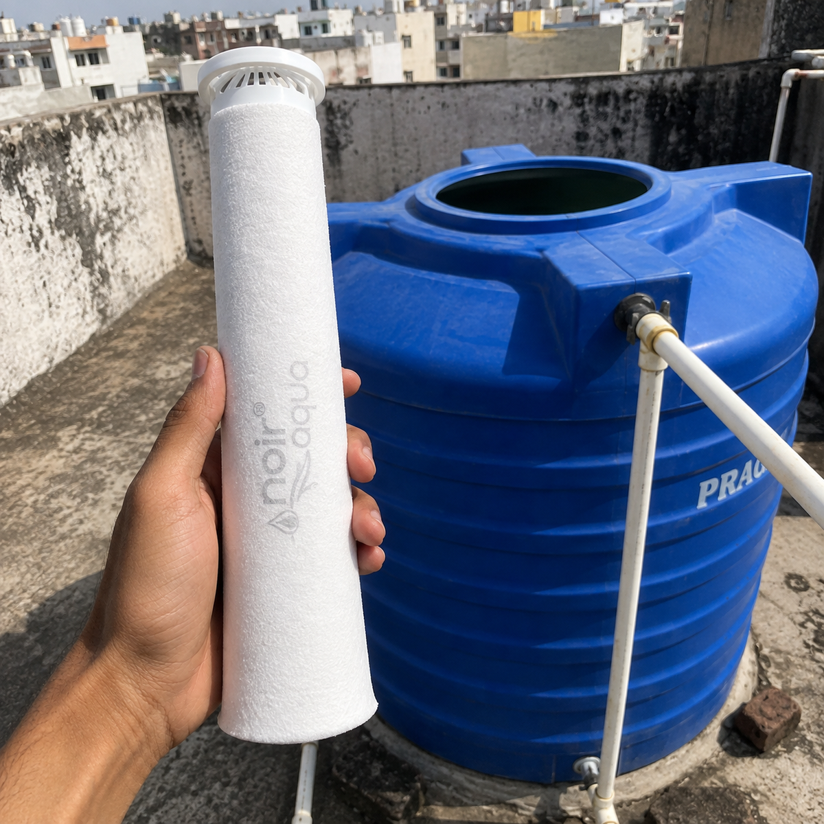 A hand holding the 20-inch filter bag beside a blue rooftop water tank