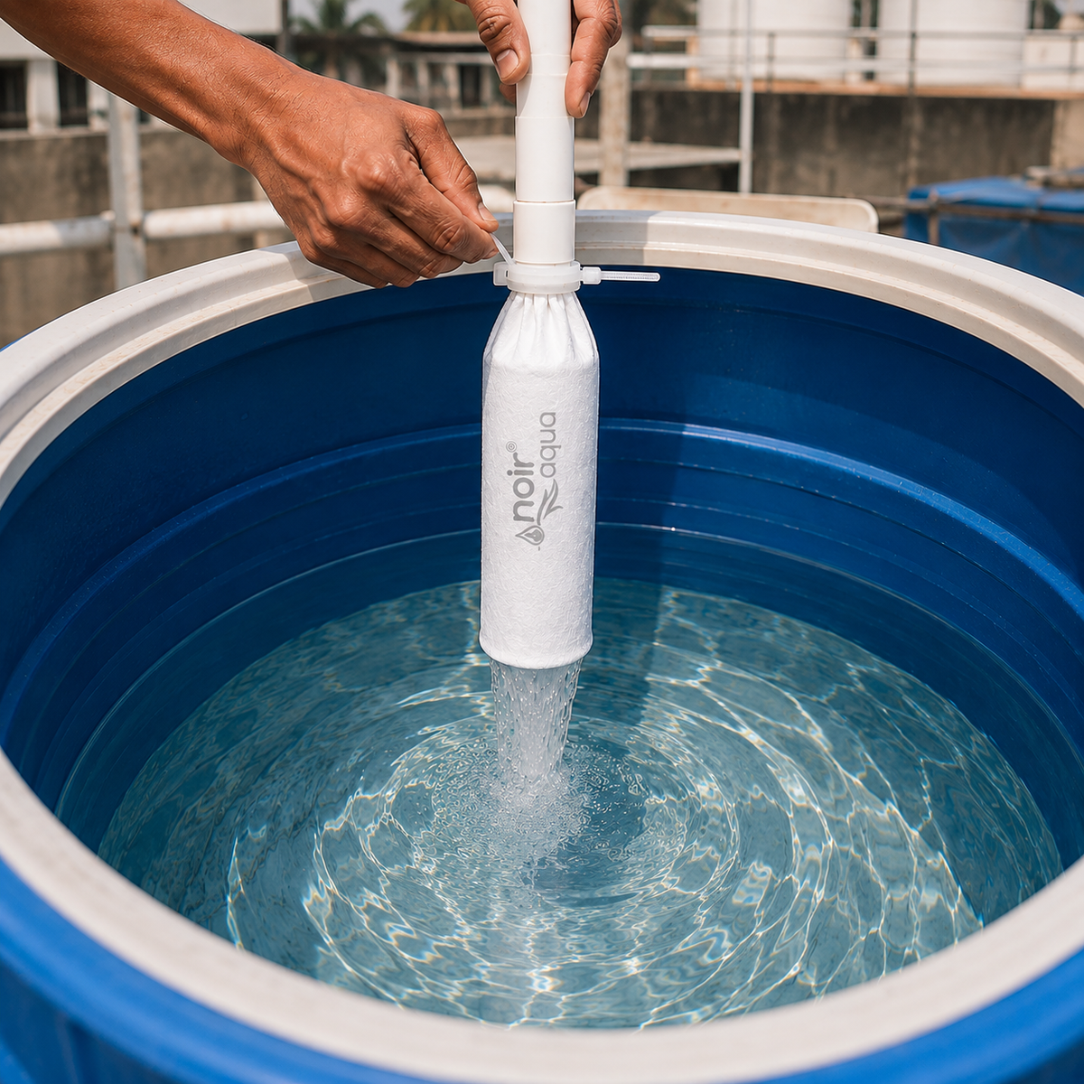 Hands tying the Noir Aqua filter bag onto the inlet pipe of a rooftop water tank as water runs through it